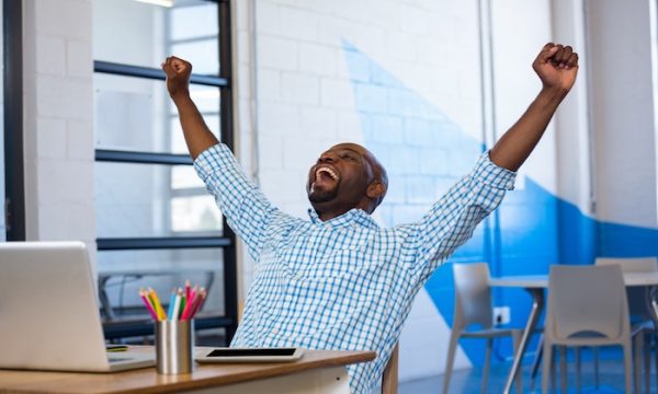 Excited man sitting on table with digital tablet and laptop